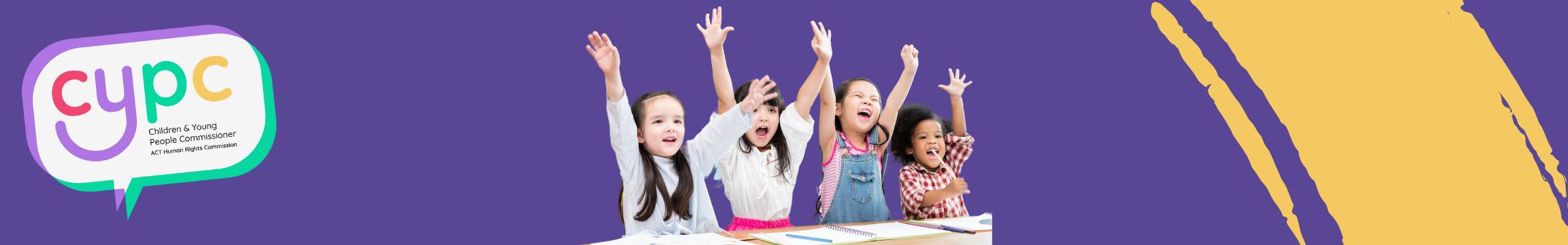 4 young children at a desk with their hands in the air